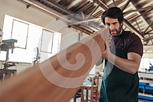 Skilled craftsman examining a plank of wood in his workshop