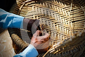 Skilled craftsman working manually a detailed bamboo wood armchair with his fingers and tools