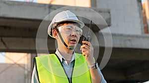 Skilled engineer inspects factory construction and uses a radio to chat with colleagues working on the field