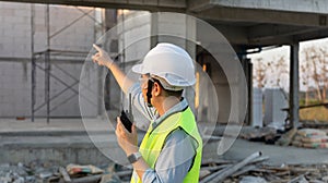 Skilled engineer inspects factory construction and uses a radio to chat with colleagues working on the field