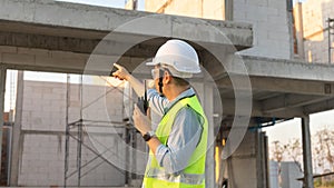 Skilled engineer inspects factory construction and uses a radio to chat with colleagues working on the field