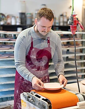 Bearded ceramicist smoothing pottery plate using belt sander photo