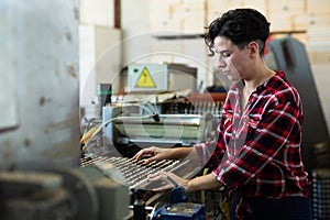 Skilled farmer woman working with automatic filling and seeding line for growing containerized seedlings of decorative