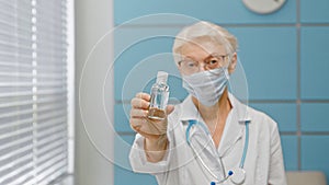 Skilled female doctor with glasses and protective mask stands in light hospital office focus on hand