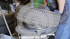 Skilled man auto mechanic puts tire on car wheel in automobile service garage.
