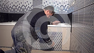 Skilled man lay tiles on bathtub side in bathroom