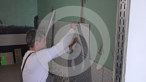 Skilled man lay tiles on wall and show finger up with smile looking at camera