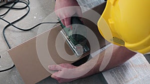 Skilled man sawing wooden laminate board with electric jig saw.