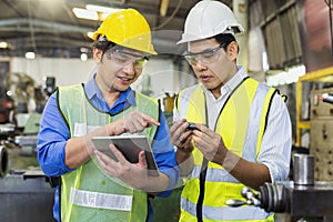 A skilled mechanic in a metal lathe is checking parts on a tablet. Engineers are working and repairing machines in industrial