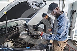 Skilled mechanics inspecting car engine using tools in a modern auto repair shop