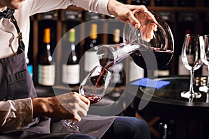 Skilled sommelier pouring wine from decanter ino wine glass.