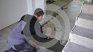 Skilled tiler apply glue and lay hexagon shape floor tiles near stairs