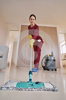 Skilled uniformed female janitor focused on mopping