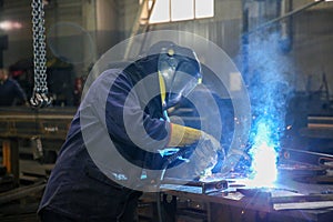 Skilled Welder in protection at Work with Sparks Flying in Industrial Workshop