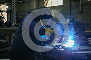 Skilled Welder in protection at Work with Sparks Flying in Industrial Workshop