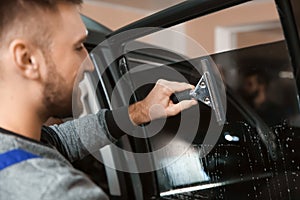 Skilled worker washing car window before tinting