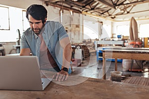 Craftsman working online with a laptop in his woodworking shop