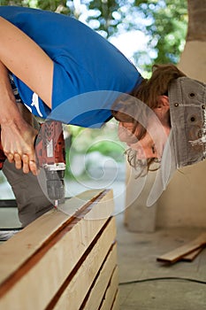 Skilled young female worker is using power screwdriver drilling during construction wooden bench gender equality