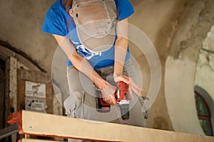 Skilled young female worker is using power screwdriver drilling during construction wooden bench gender equality