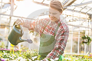 Skilled young man watering houseplants while working as florist