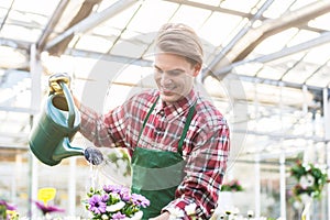 Skilled young man watering houseplants while working as florist