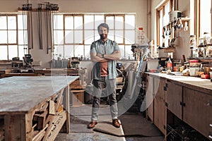 Skilled young woodworker standing in his workshop full of tools