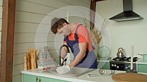 Skillful African American plumber installing kitchen faucet with wrench