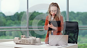 Skillful female architect with dreadlocks near mockup of house and analysing technical documents. photo