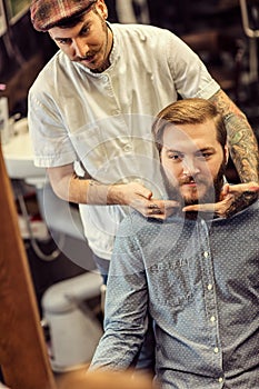 Skillful barber making haircut too bearded customer