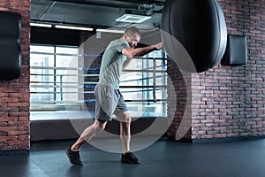 Skillful boxer beating punching bag while training in gym