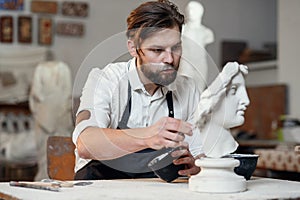 Skillful sculptor makes professional restauration of gypsum sculpture of woman`s head at the creative workshop. photo