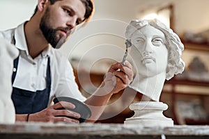 Skillful sculptor makes professional restauration of gypsum sculpture of woman`s head at the creative workshop. photo