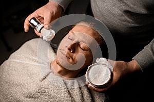 Skillfull barber applying shaving foam onto client& x27;s face using old-fashioned shaving brush