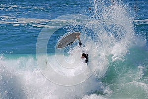 Skim Boarder wiping out while riding a shore break wave at Aliso Beach in Laguna Beach, California.