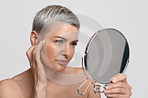 Skin Aging. Mature woman looking in the mirror checking her wrinkles