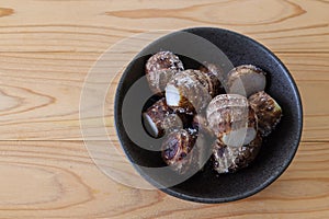 Skin-on boiled taro corm in a black crockery on a wooden table.