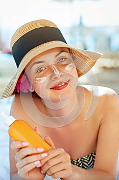 Skin care. Beauty Concept. Young pretty woman holding  sun cream and applying on her face. Female in hat smear  sunscreen lotion