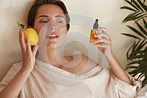 Skin Care. Beauty Portrait Of Woman Holding Lemon And Bottle Near Face. Natural Cosmetic Product For Hydrated Derma.