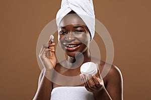 Skin Care Concept. Young Black Lady Applying Moisturizing Face Cream After Bath