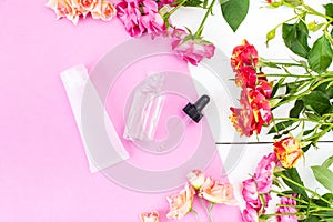 Skin Care Cosmetics in a Frame of Fresh Roses. Essence, Oil on a pink and white desk photo