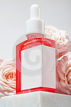 Skin care face serum bottle surrounded by pink rose flowers on marble podium, unbranded bottle with blank label for