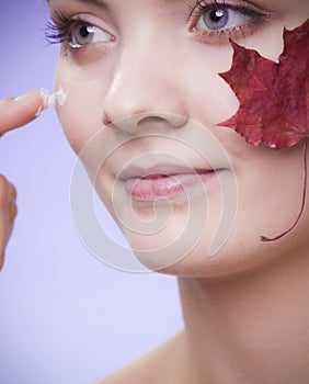 Skin care. Face of young woman girl with red maple leaf.