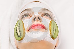 Skin care, facial mask and cosmetology concept. Close up macro of face of pretty woman with mud facial mask and kiwi