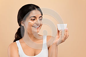 Skin Care. Happy Attractive Indian Lady Holding White Jar With Moisturising Cream