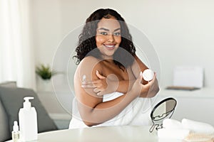Skin care. Pretty bodypositive woman applying moisturising body lotion after bath, standing with cosmetic jar in hand