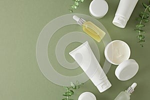 Top view photo of white cosmetic tube, cream jar, dropper bottles and eucalyptus leaves on pastel green background
