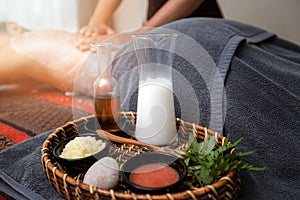 Skin care products and a cosmetic body scrub in basket with Spa therapist applying scrub salt and cream on woman back. Beauty