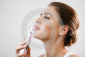 Skin Care. Side portrait of the charming healthy fresh woman with natural make-up using the electric facial massager at