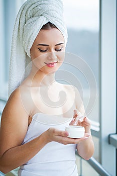 Skin care. Studio shot of beautiful young woman applying moisturizer cream onto her face