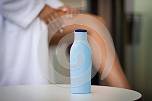 Skin care during summer concept: close-up a bottle of cream and woman applying body lotion on her legs